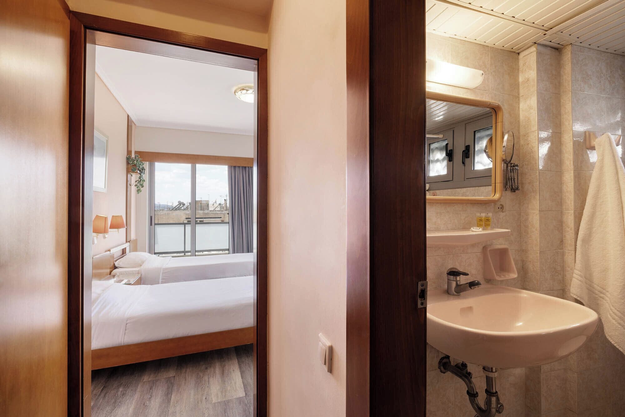 Habitación de hotel con cama, baño con lavamanos y vistas a la ciudad desde la ventana.