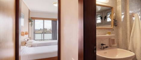 Habitación de hotel con cama, baño con lavamanos y vistas a la ciudad desde la ventana.