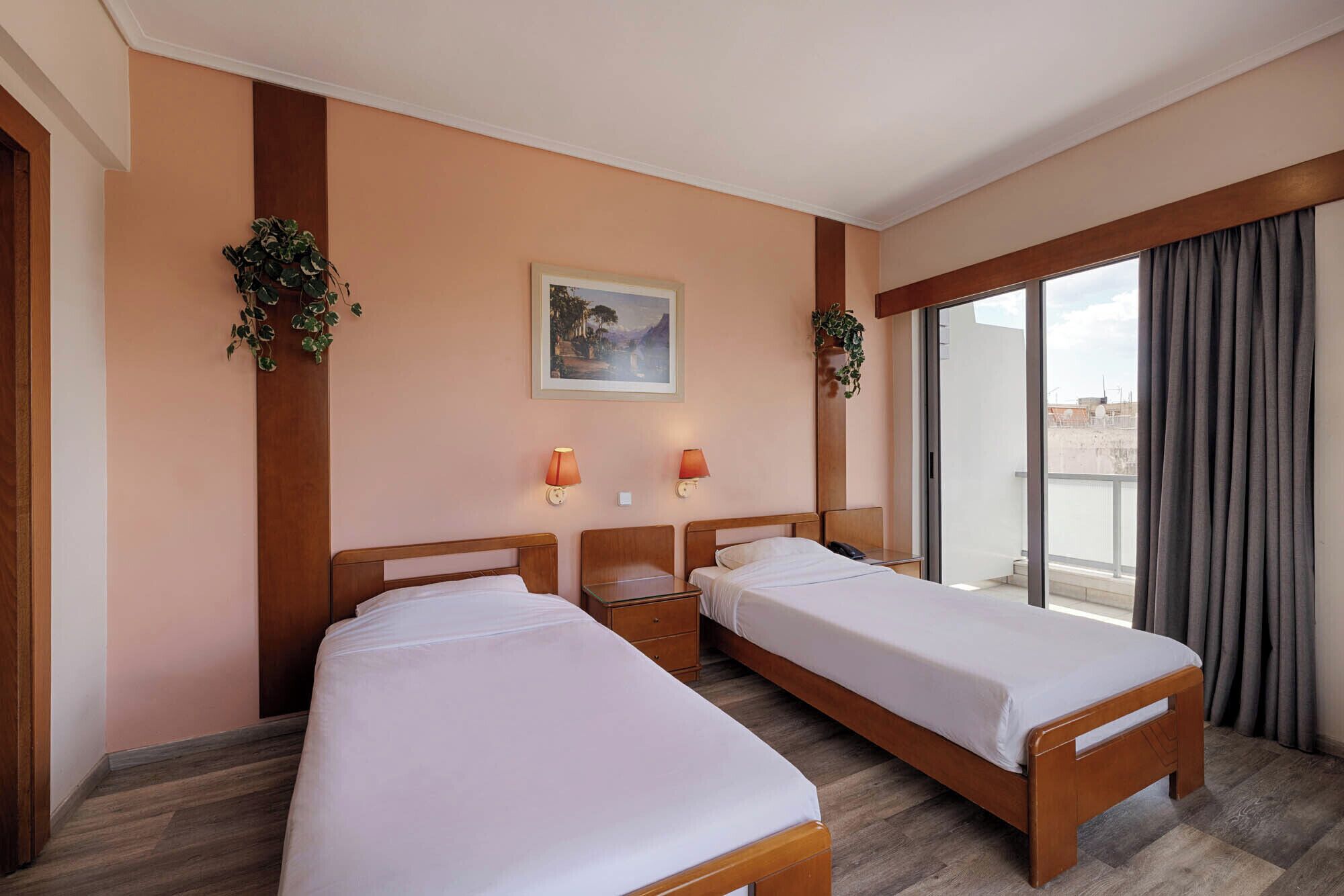 A hotel room with two beds, a large window with curtains, a painting on the wall, and two wall-mounted lamps.