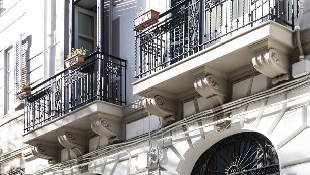 A building facade with a large arched entrance, a dark wooden door, and a balcony with potted plants. - Principe di Belmonte (Palermo)
