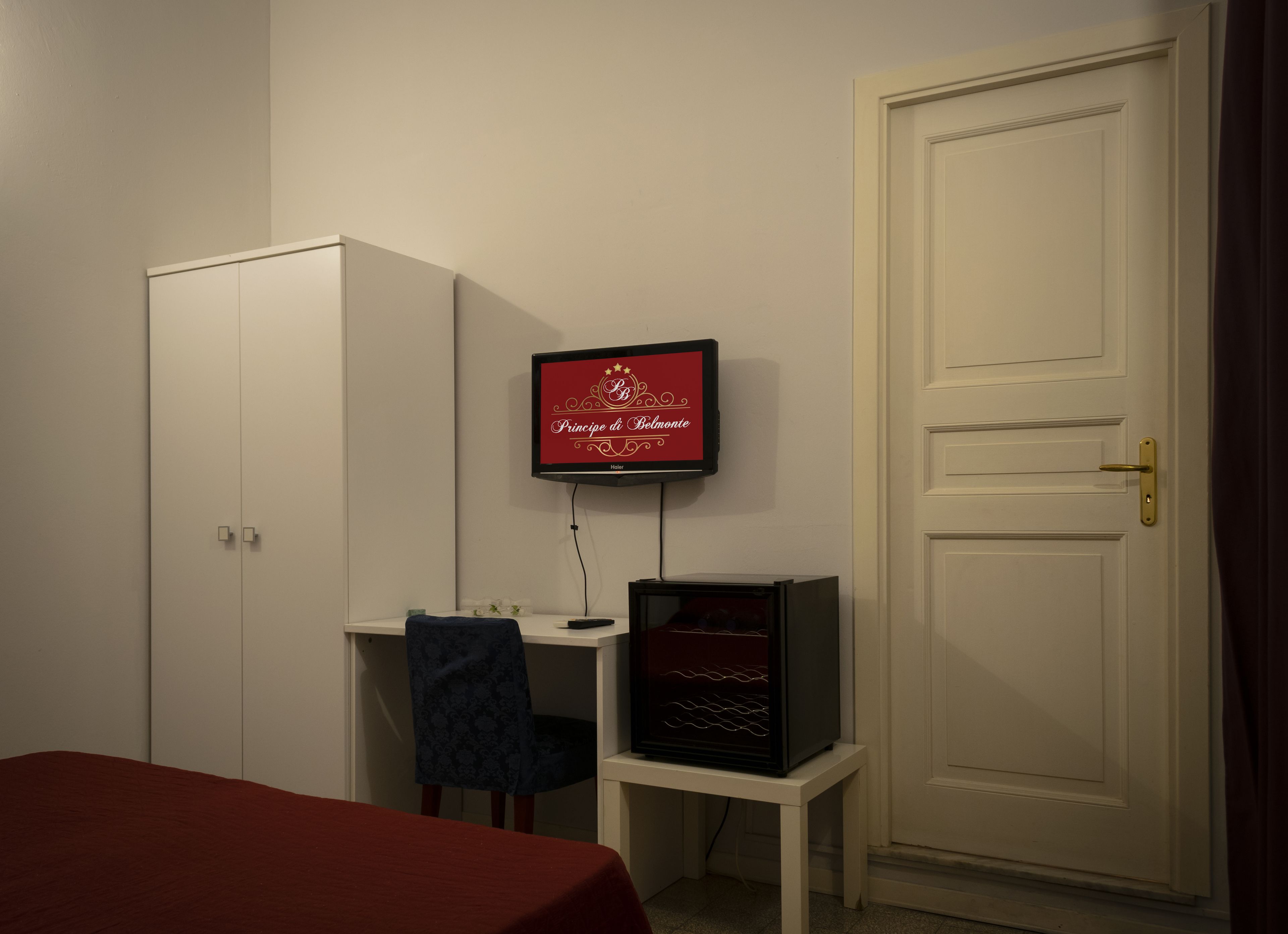 Une pièce comprenant un lit, un bureau avec un ordinateur, une télévision et une porte.