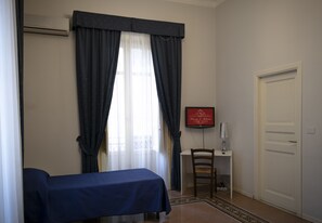 A hotel room with a bed, a desk, a chair, a TV, and a door. - Principe di Belmonte (Palermo)