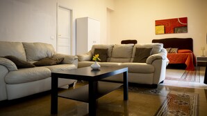 A living room with a sofa, a coffee table, a cabinet, and a bed with an orange bedspread. - Principe di Belmonte (Palermo)