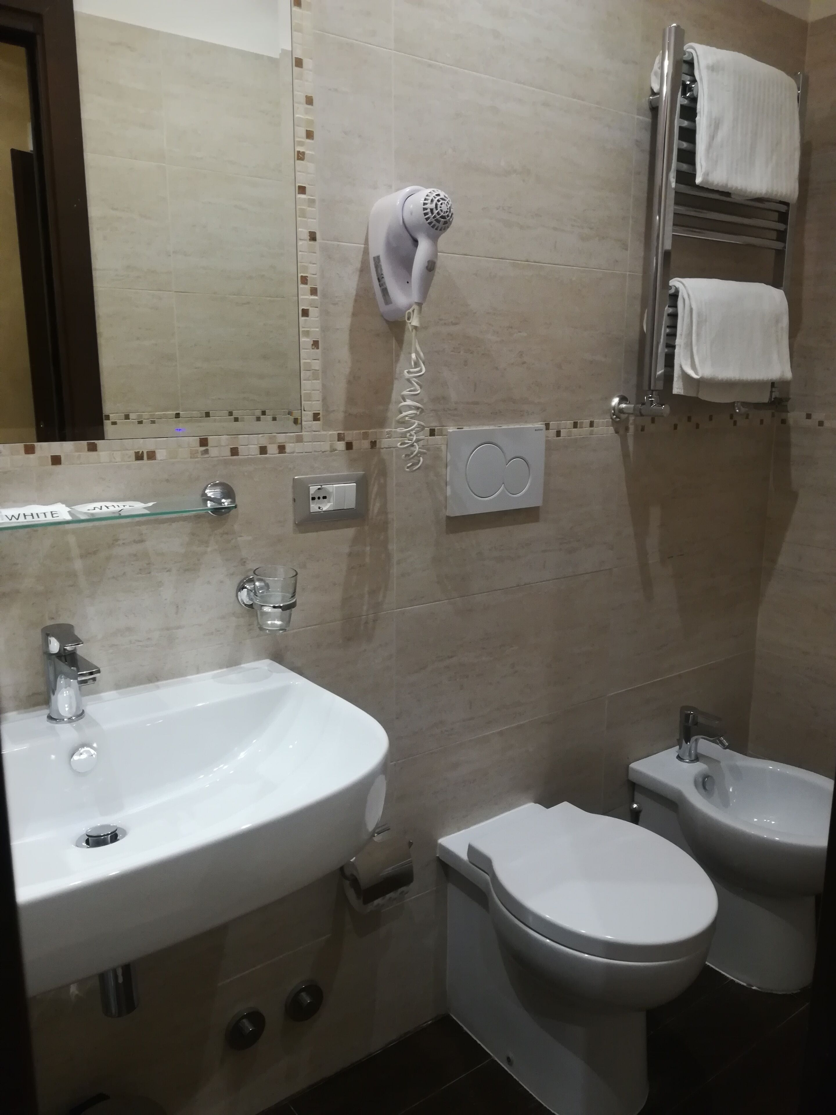 Une salle de bain équipée d’un lavabo, de toilettes, d’un bidet, d’un porte-serviettes et d’un sèche-cheveux.