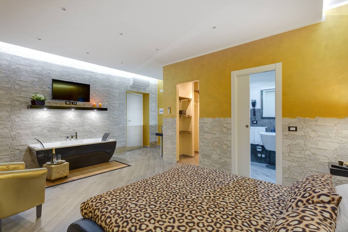 A modern bedroom with a stone wall, a large bed with leopard print bedding, a built-in desk, and a TV mounted on the wall.