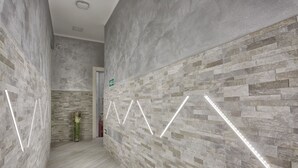 A hallway with textured stone walls and a modern light fixture. - Excellence Suite (Rome)