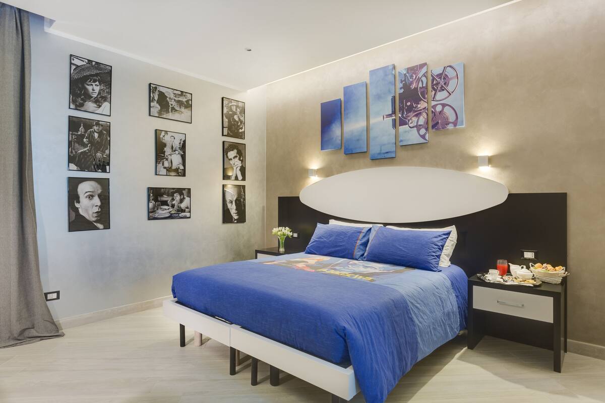 A modern bedroom with a large bed, a nightstand, and a wall with framed pictures.