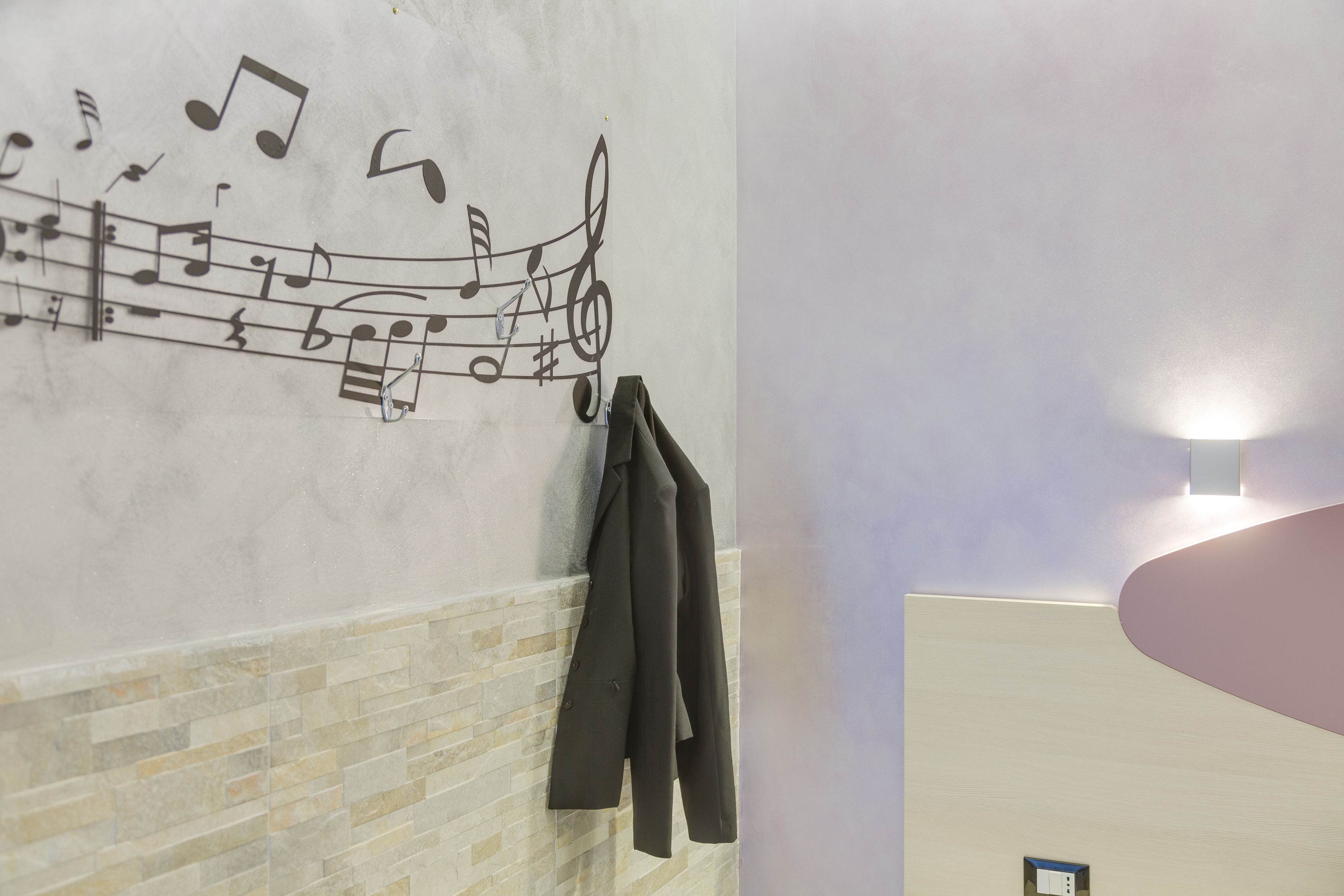 Un baño con pared de azulejos, un perchero con una chaqueta y una lámpara.