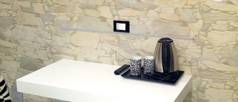 A modern room with a flat-screen TV mounted on the wall, a white desk with a kettle, a zebra-patterned chair, and a small heater.