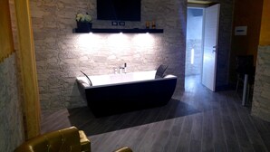A modern bathroom with a stone wall, a large mirror, and a built-in sink. - Excellence Suite (Rome)
