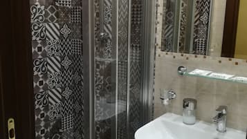 A bathroom with a glass shower enclosure, a white sink, and patterned tiles.