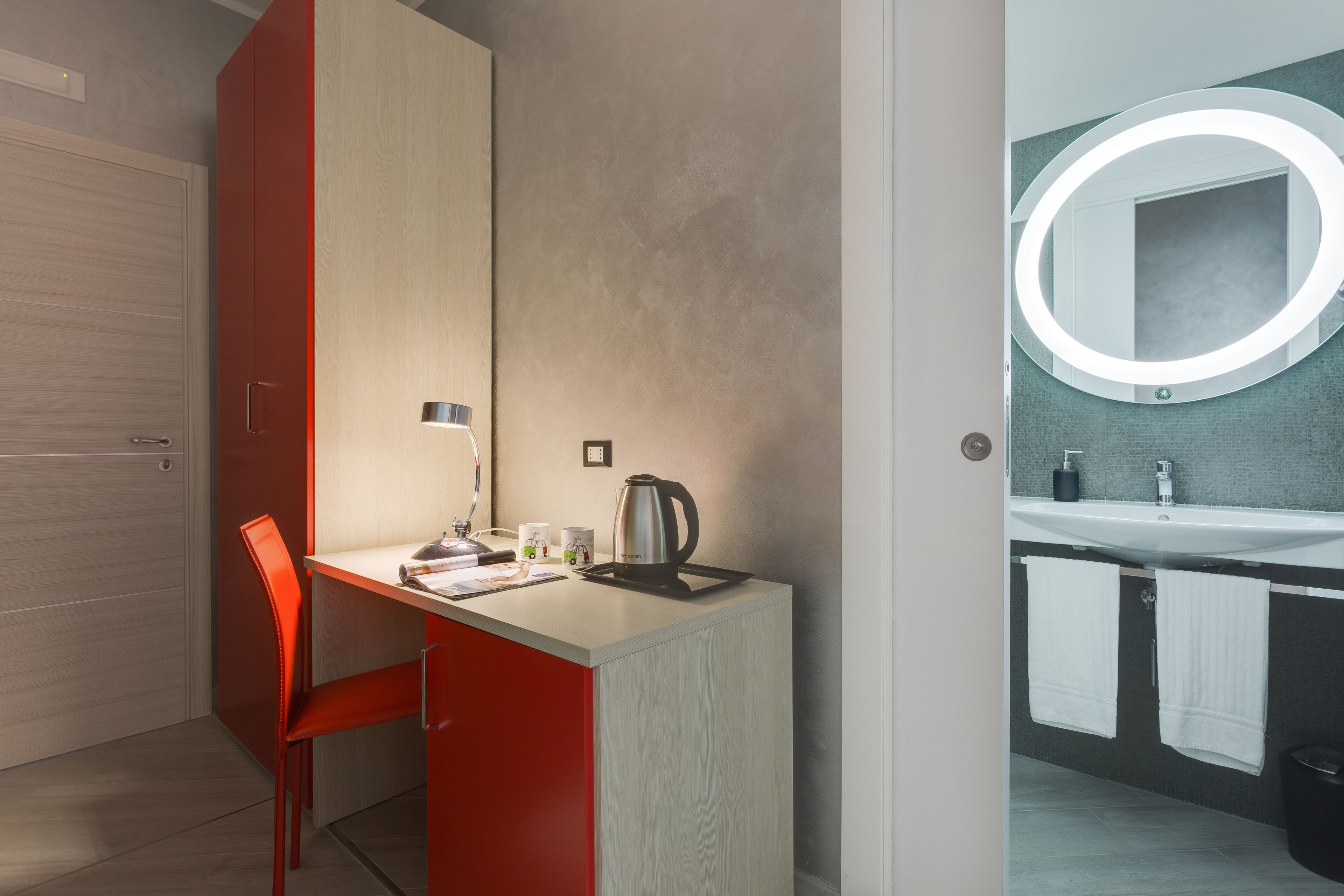 A modern room with a desk, chair, and a bathroom with a sink and mirror.