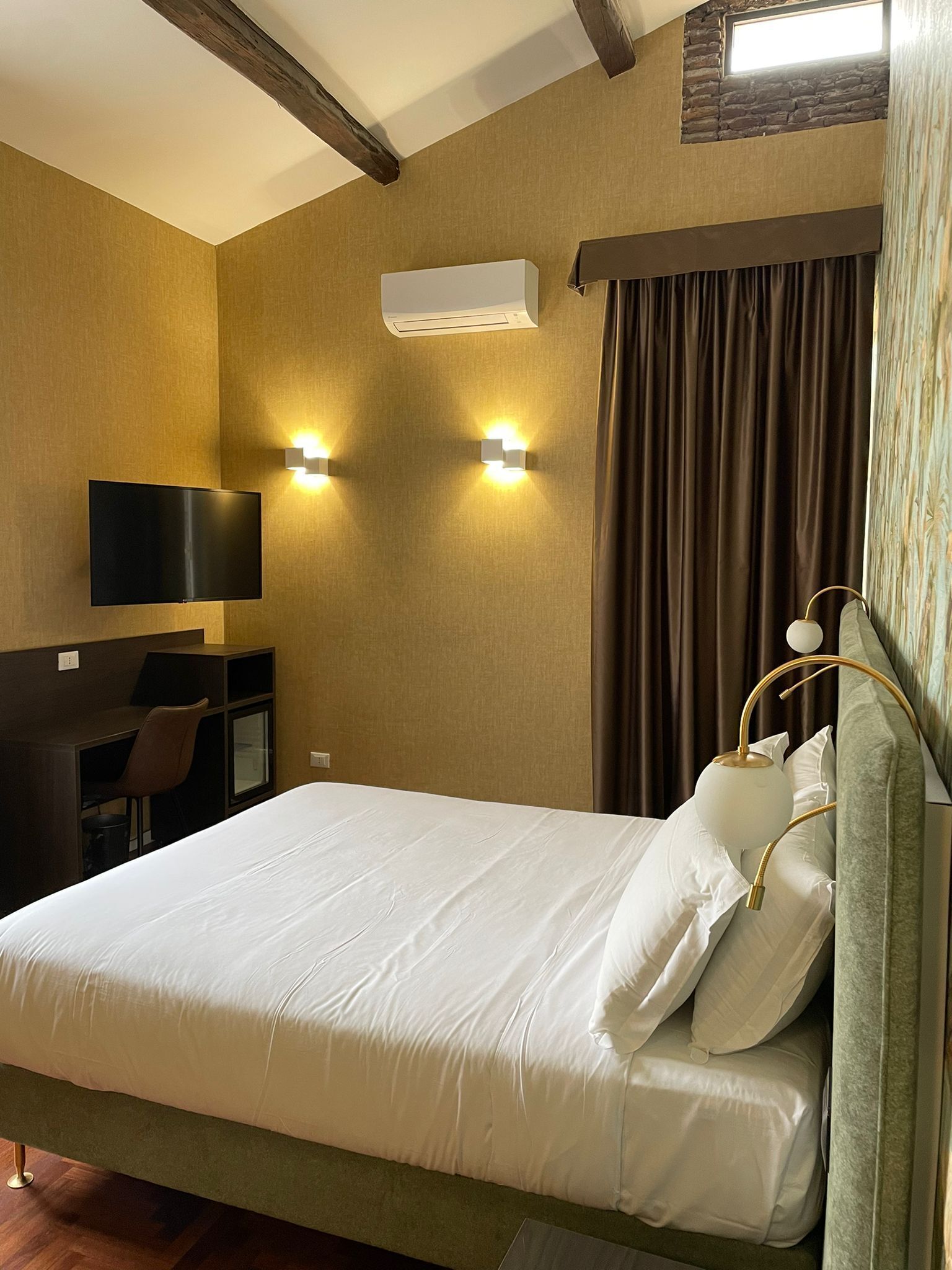 Une chambre d’hôtel comprenant un lit, un bureau avec une chaise, un téléviseur à écran plat et deux lampes fixées au mur.