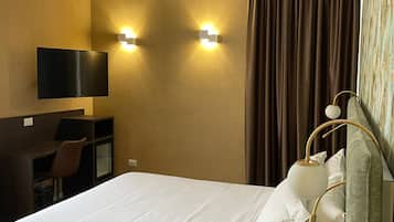 Habitación de hotel con cama, escritorio con silla, televisor de pantalla plana y dos luces fijadas a la pared.