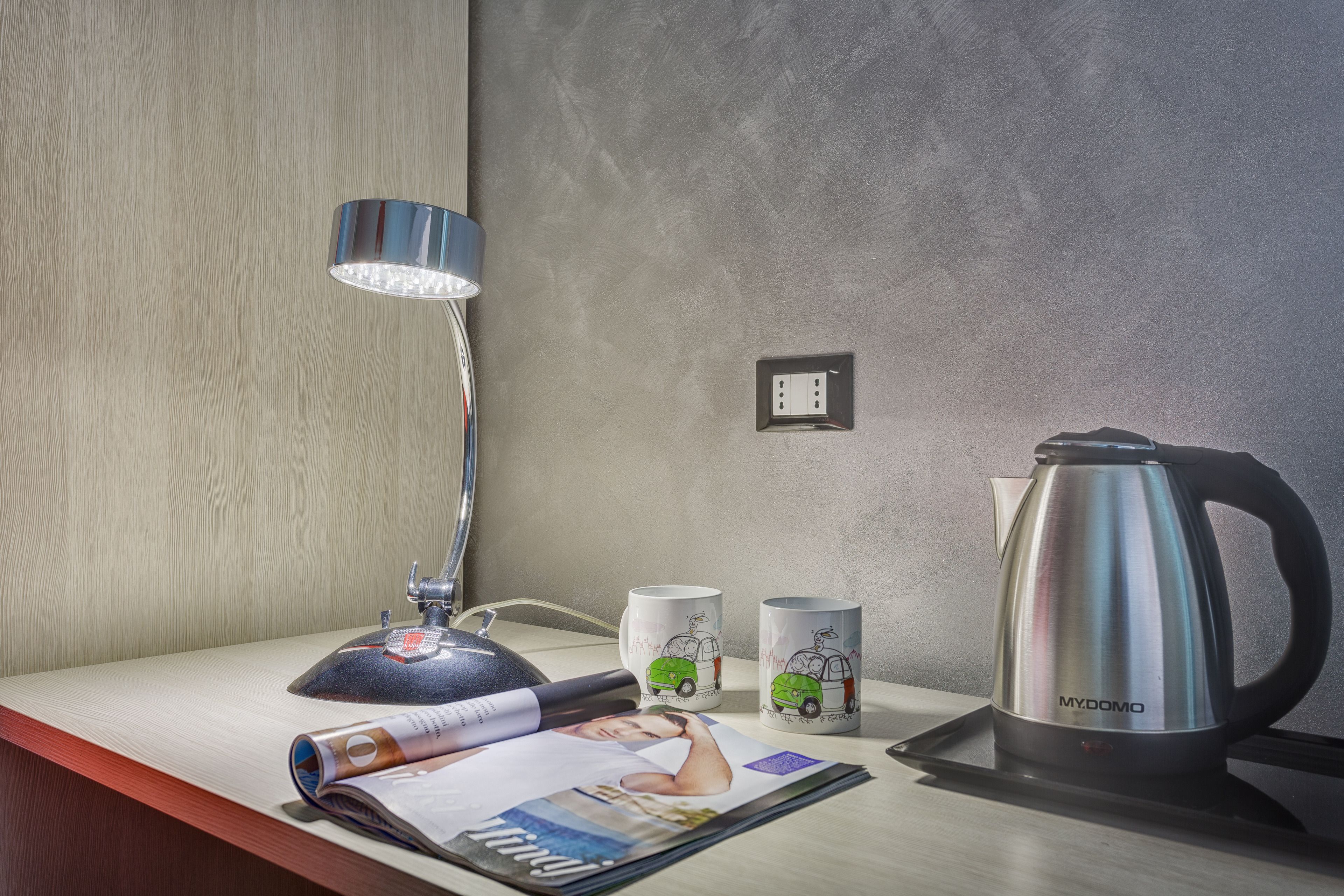 Uma mesa com uma luminária, duas canecas, uma chaleira e uma revista.