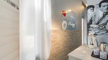 A bathroom with a shower curtain, a wall-mounted towel rack, a towel, a sink with a mirror, and a coffee maker.