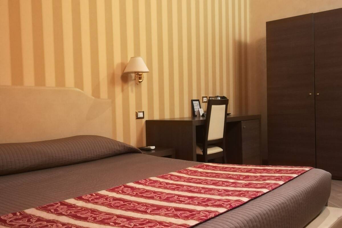 A hotel room with a large bed, a desk, and a wardrobe.