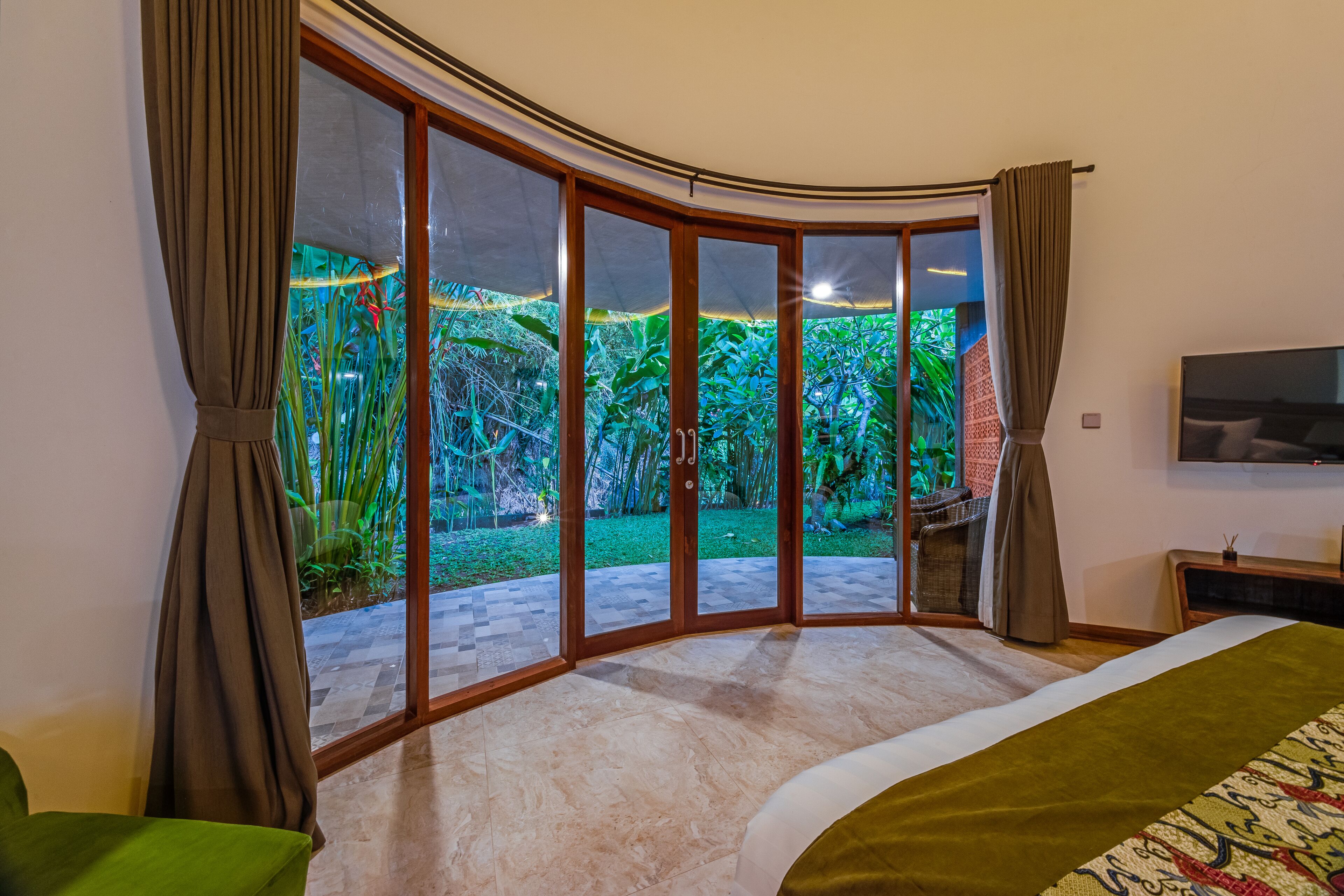 A bedroom with a curved glass door leading to a garden.