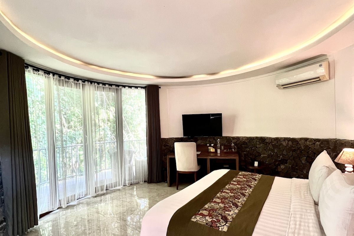 Ein Hotelzimmer mit einem großen Bett, einem Schreibtisch, einem Sessel, einem Fernseher und einer Wand mit Steinverkleidung.