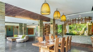Een ruime eethoek met een houten tafel en stoelen, omgeven door stenen zuilen en uitzicht op groen.