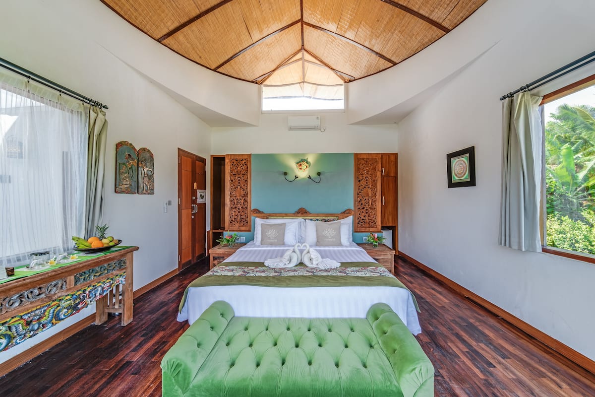 Ein geräumiges Schlafzimmer mit einem großen Bett, einer grünen Polsterbank, einem Holznachttisch und einem dekorativen Tisch.