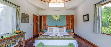 A spacious bedroom with a large bed, a green upholstered bench, a wooden nightstand, and a decorative table.