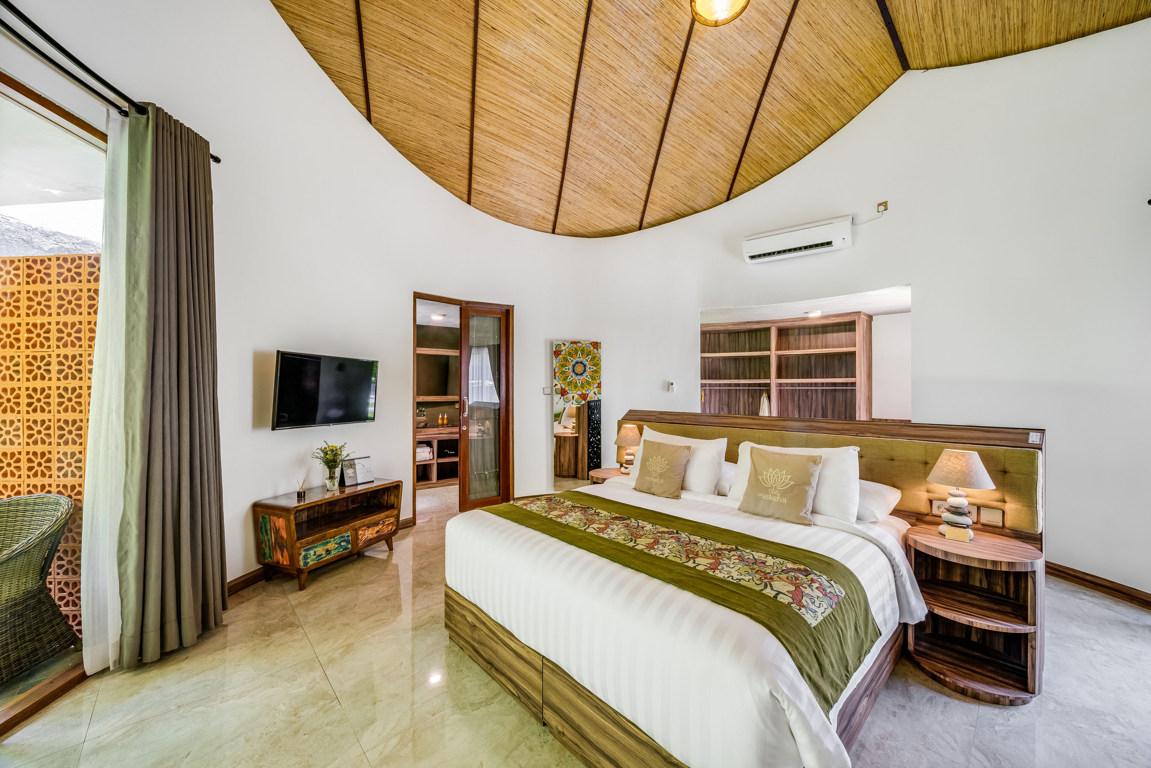 A bedroom with a large bed, a TV, a wooden headboard, a nightstand, and a window with curtains.