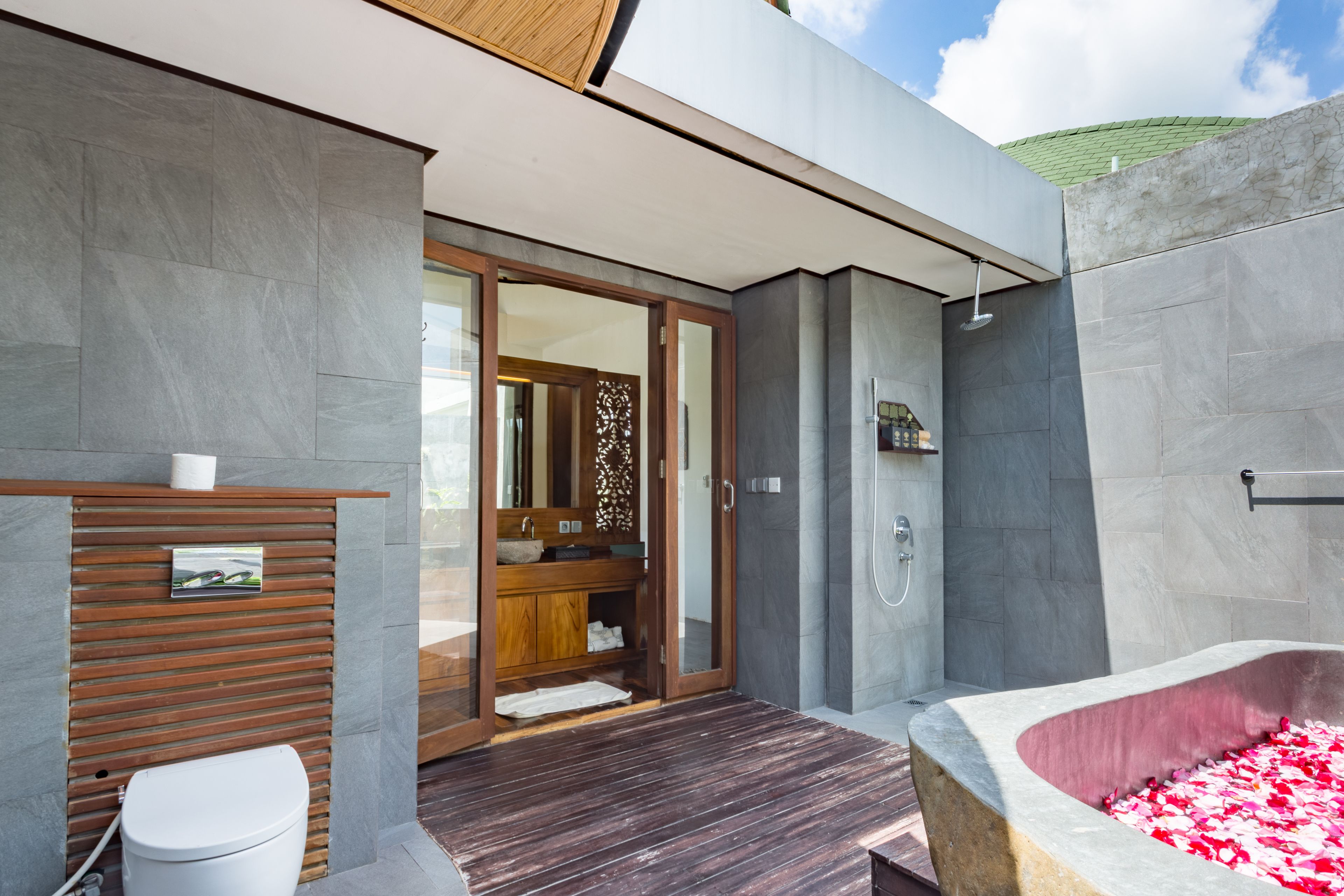A modern bathroom with a wooden vanity, a large bathtub with rose petals, and a shower area.