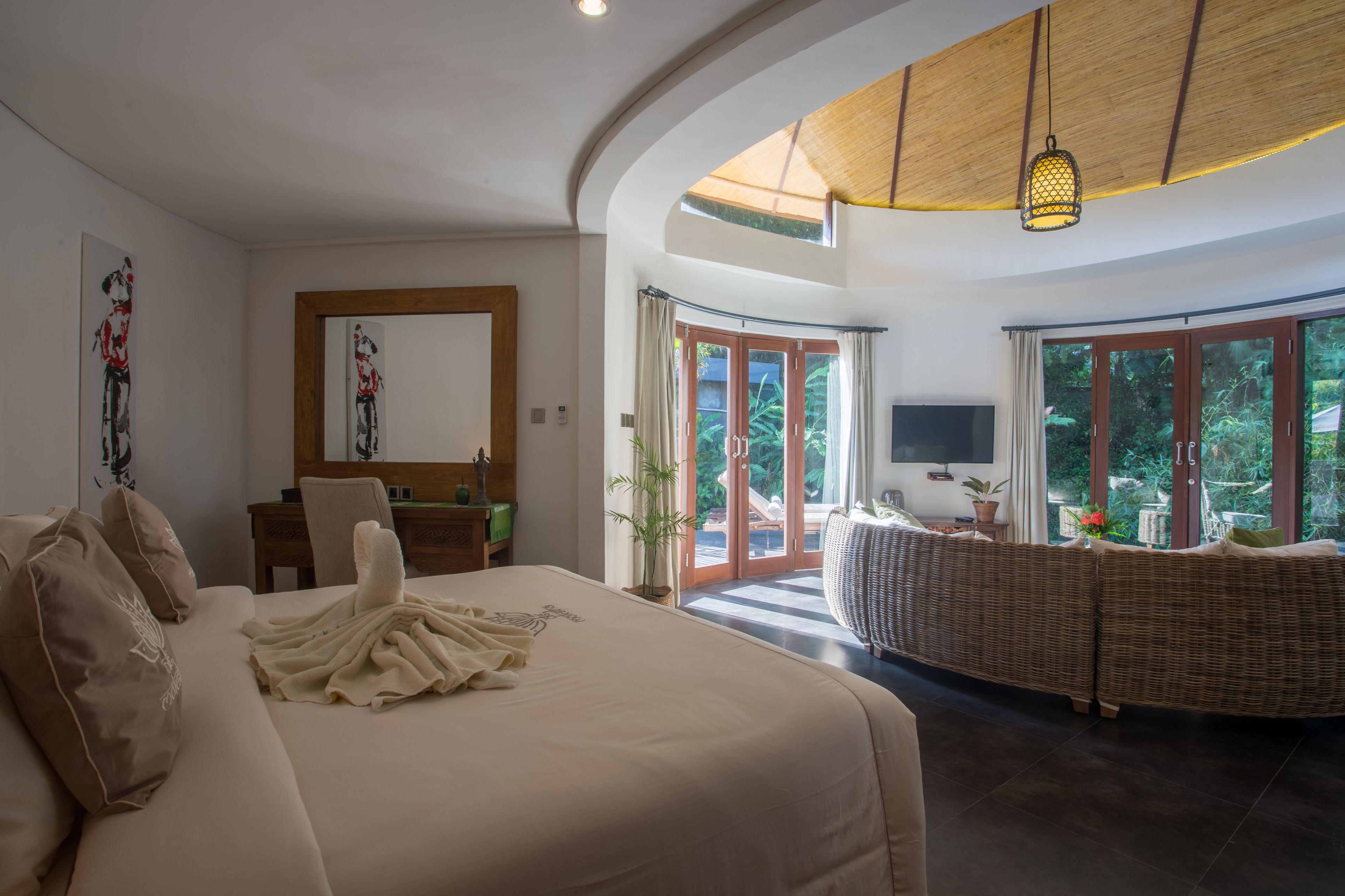 A spacious bedroom with a large bed, a desk, and a wicker sofa.