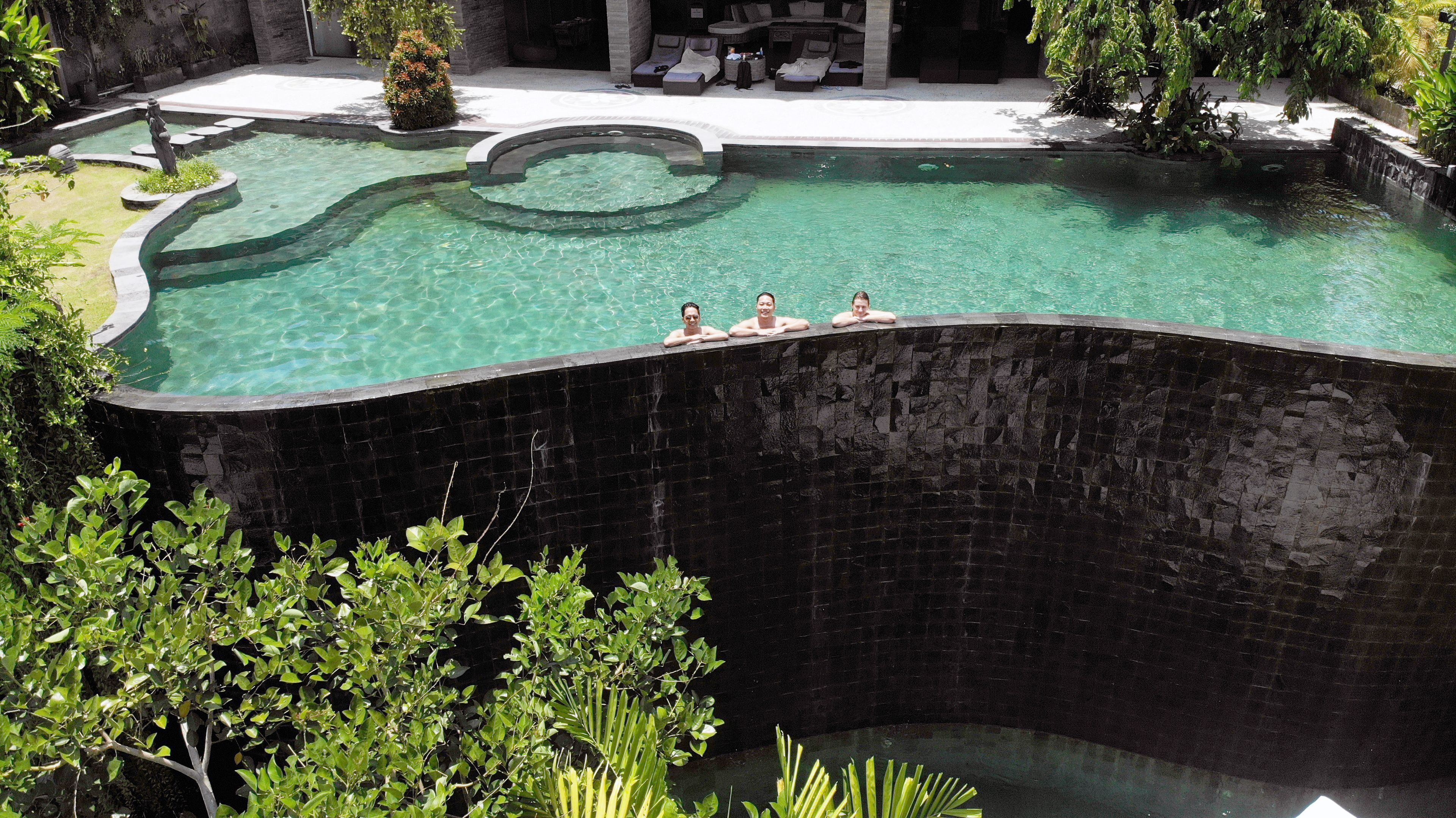 A swimming pool with a curved edge, surrounded by greenery and a lounge area with seating.