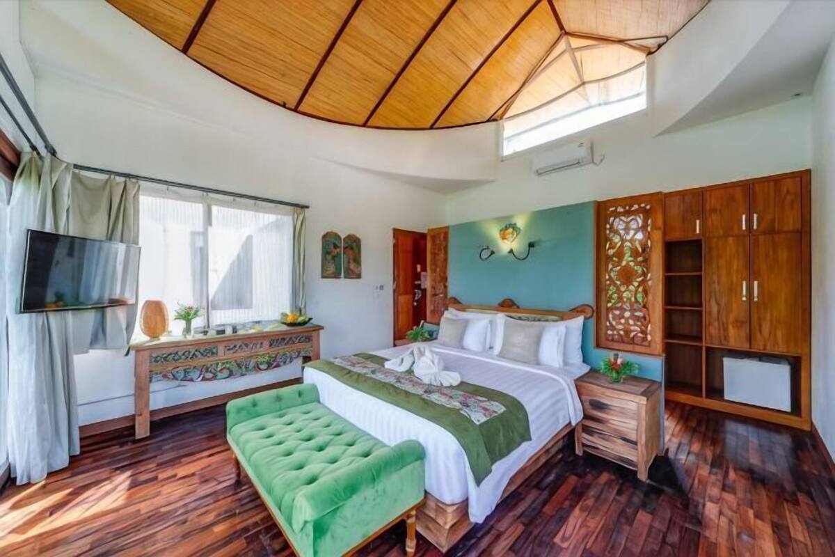 Ein Schlafzimmer mit einem Bett, einer grünen Bank, einer Holzbalkendecke, einem Fernseher und einem Kleiderschrank.