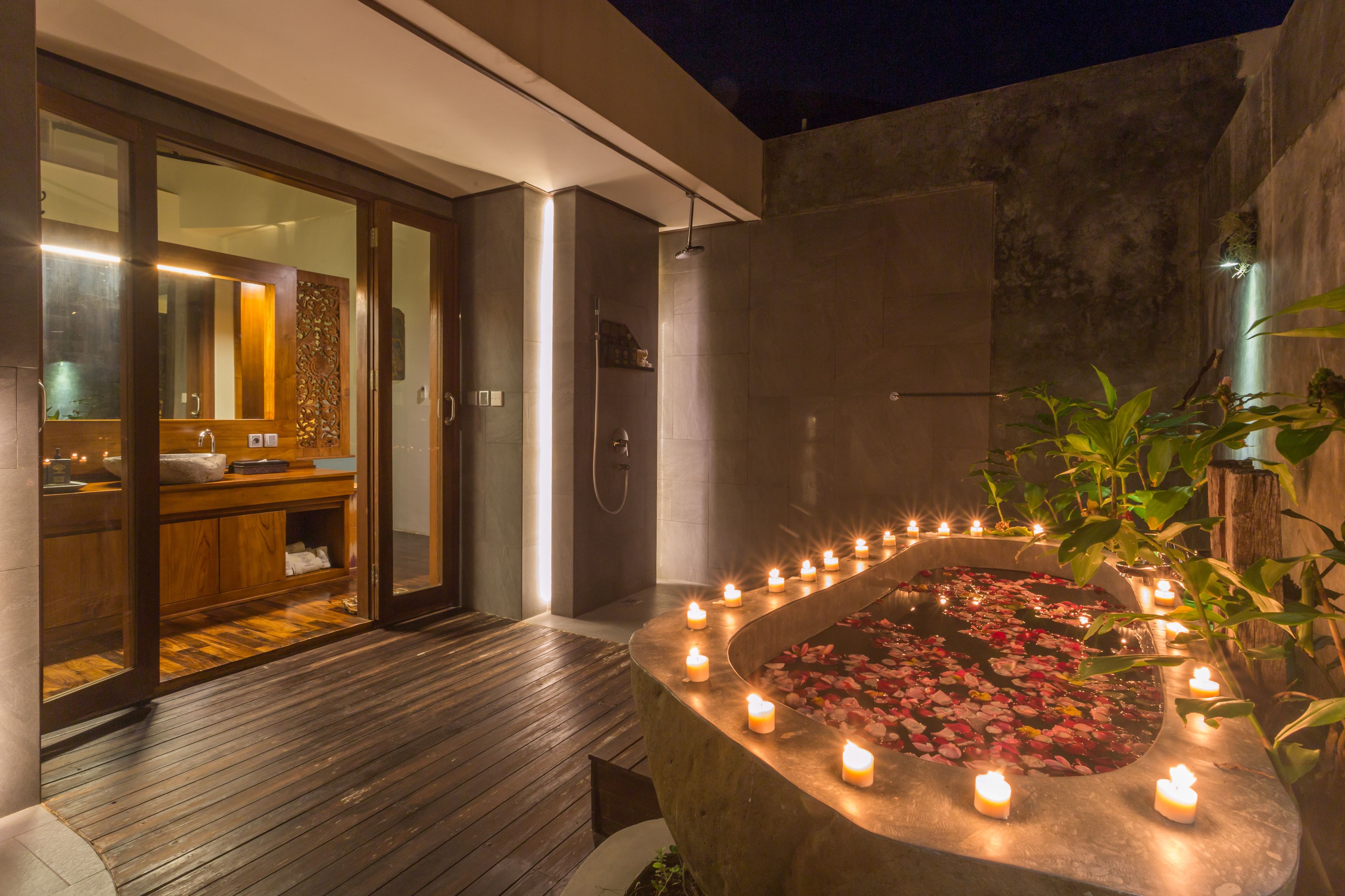 A modern bathroom with a wooden vanity, a glass shower enclosure, and a stone bath surrounded by candles.