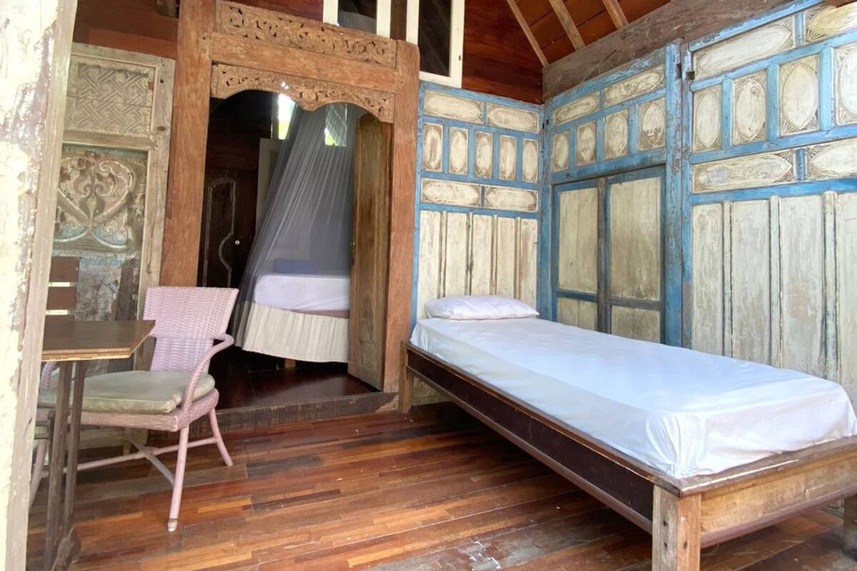 A rustic wooden room with a single bed, a chair, and a small table.