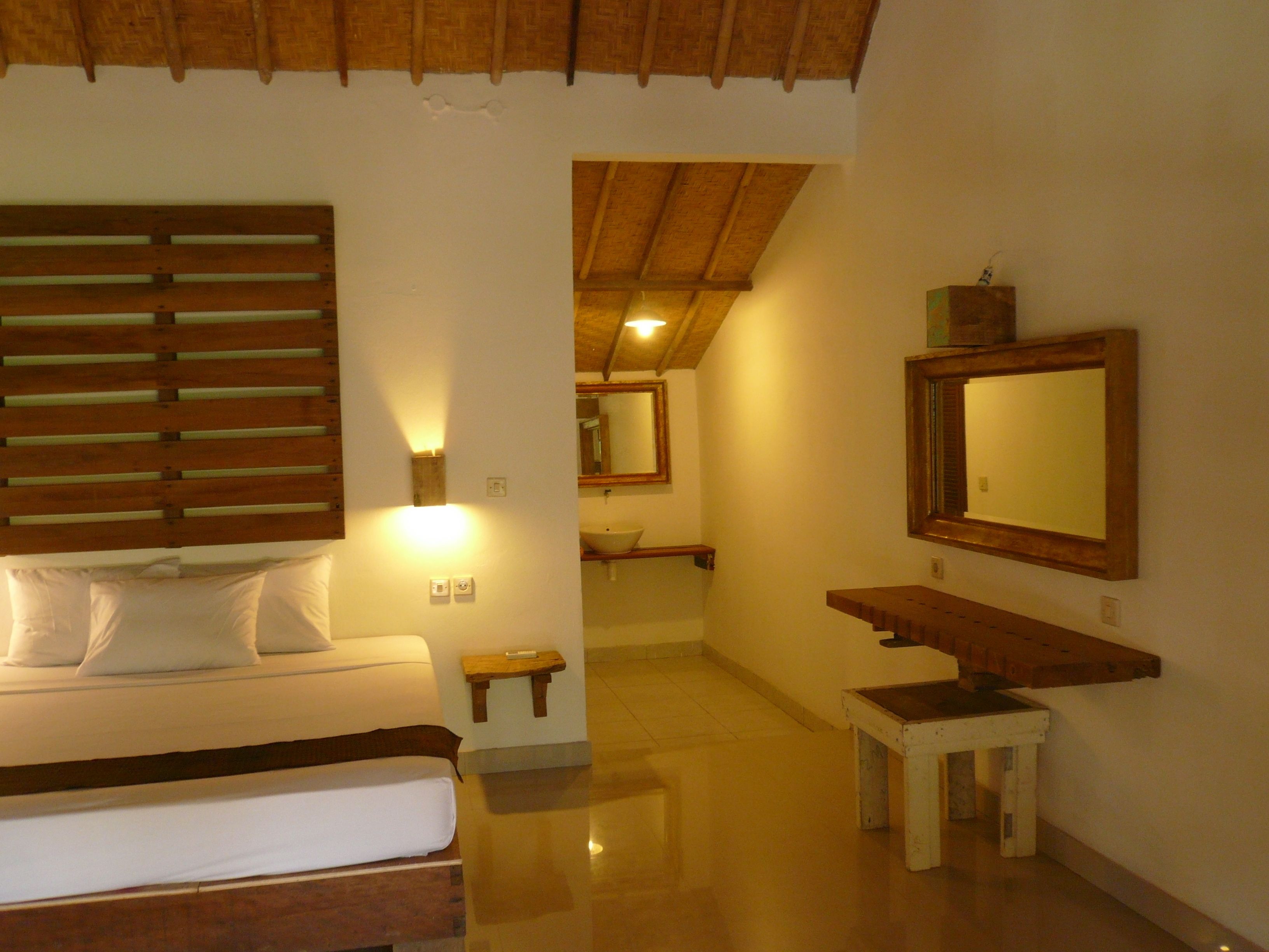 Quarto com cama, mesa de cabeceira e espelho na parede.