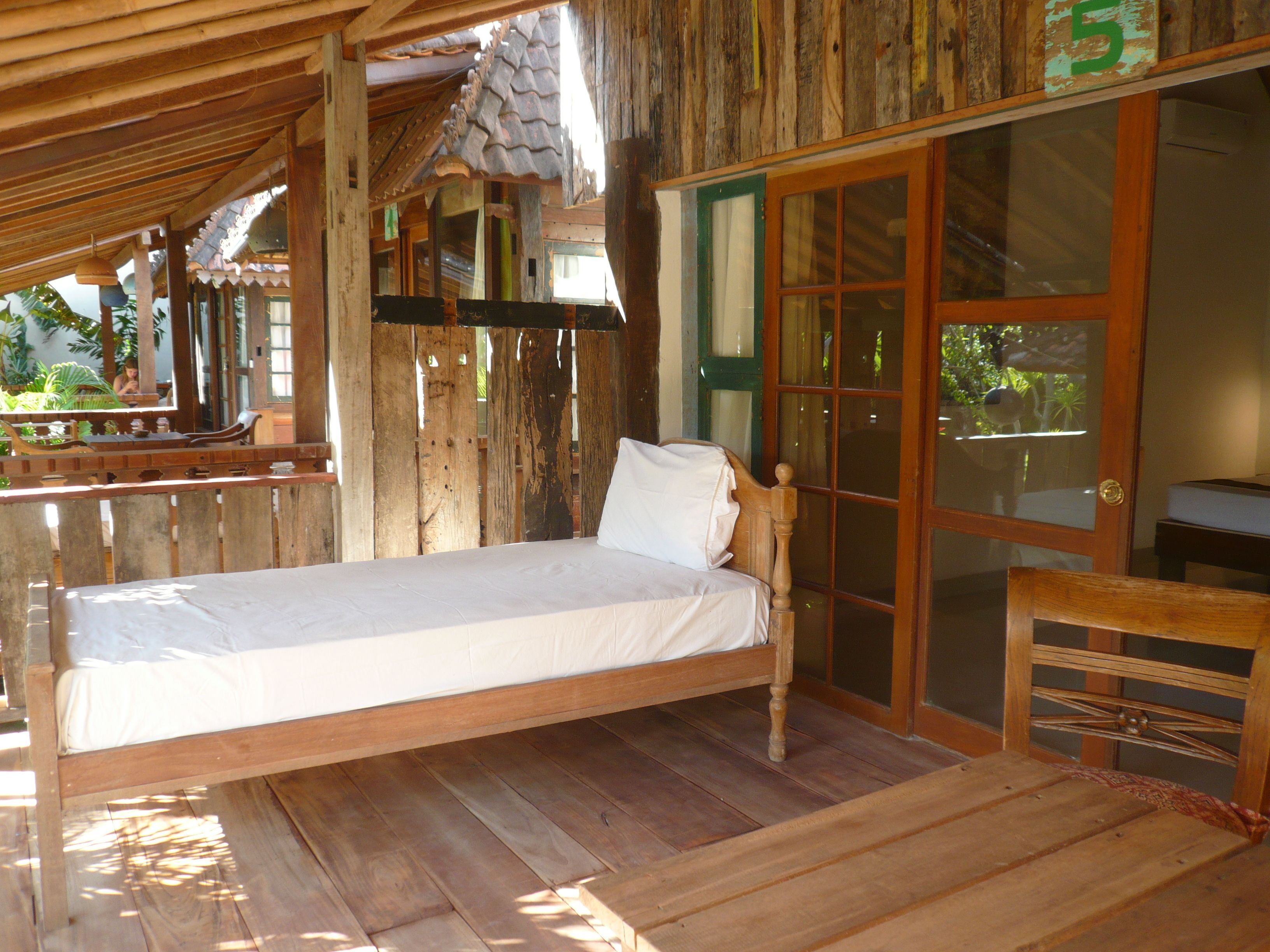 A wooden bed in a rustic room with a balcony, a wooden chair, and a sliding glass door.
