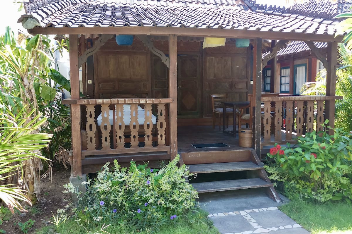 A wooden structure with a tiled roof, a porch with a railing, and a small table with chairs.