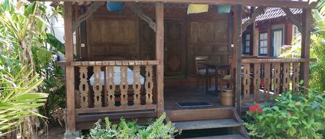 A wooden structure with a tiled roof, a porch with a railing, and a small table with chairs.