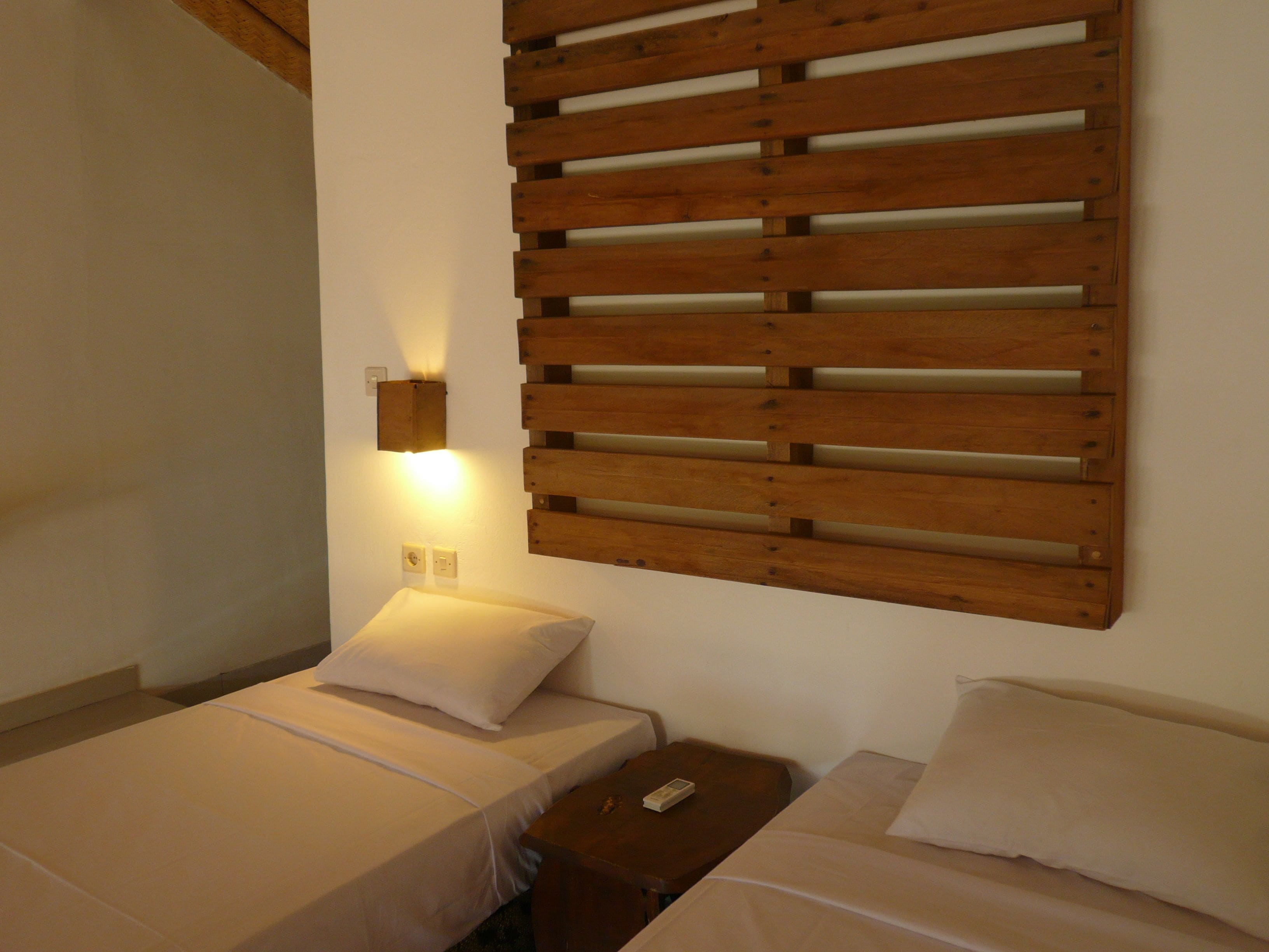 Ein Schlafzimmer mit zwei Betten, einem Holzschrankgitter-Kopfstück, einem Nachttisch und einer Wandleuchte.