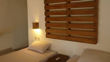 Ein Schlafzimmer mit zwei Betten, einem Holzschrankgitter-Kopfstück, einem Nachttisch und einer Wandleuchte.