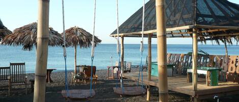 A beachside swing area with bamboo poles, a covered seating area, and a view of the sea.