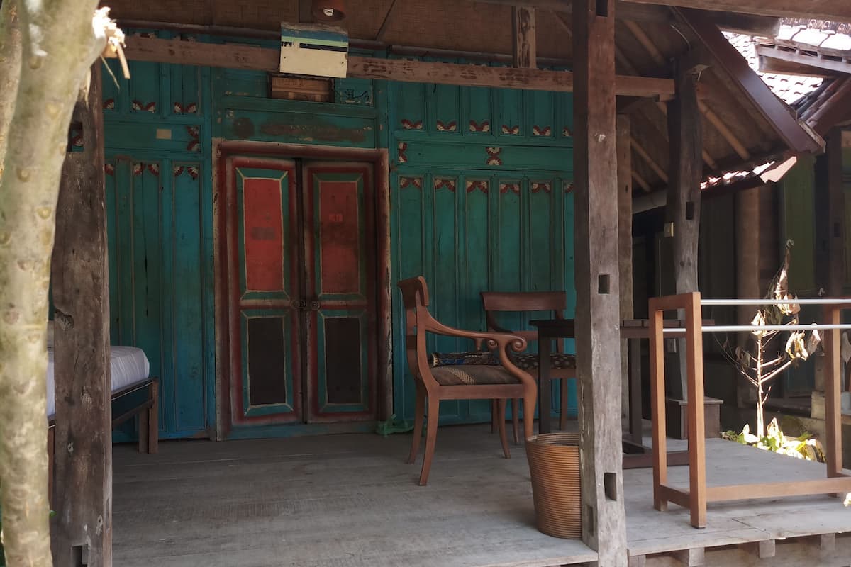 A wooden porch with a bench and a chair, a trash bin, and a wooden structure with a metal frame.