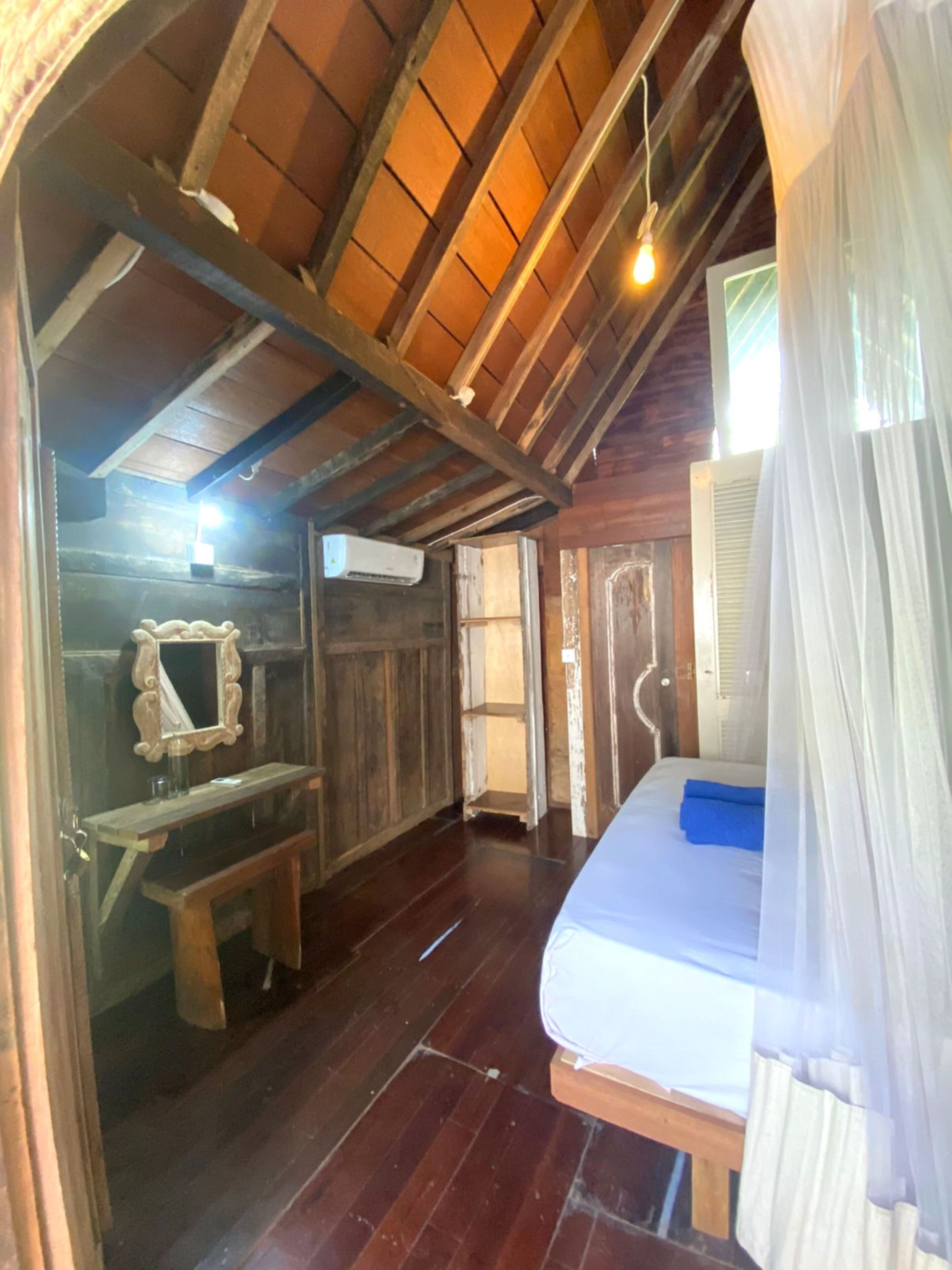 A rustic wooden room with a bed, a bench, and a mirror.