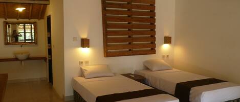 Habitación de hotel con dos camas, cabecero de madera con listones, un espejo grande, un lavamanos y una ventana.