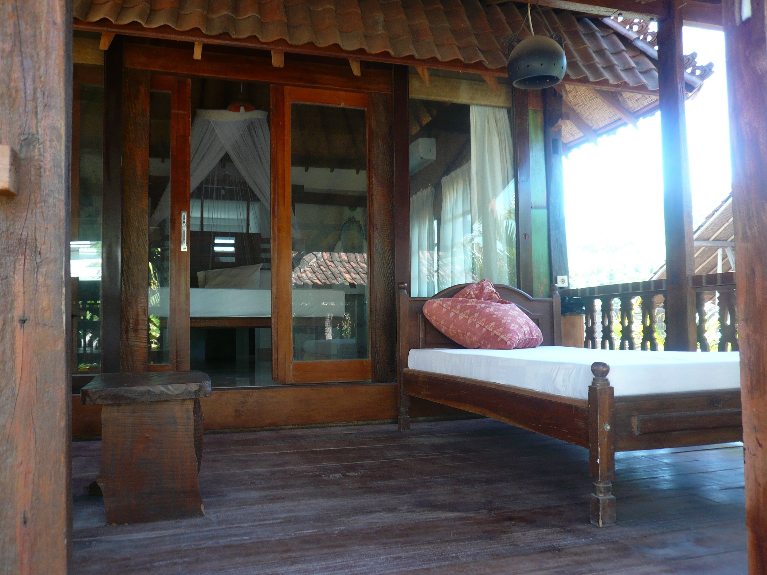 A wooden bed with a mattress and pillows on a balcony with a wooden floor.