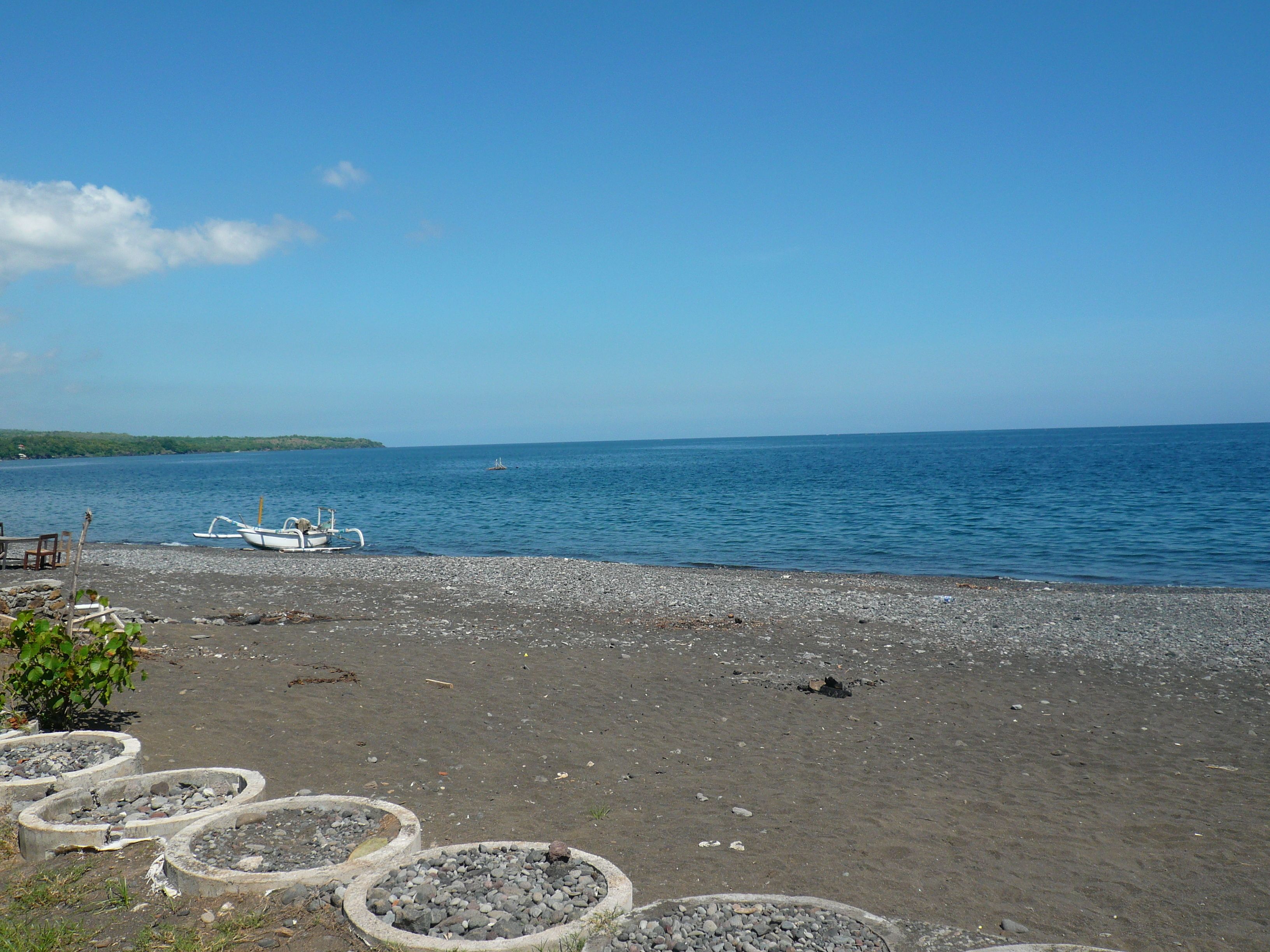 A pebbled beach with boats, a clear sky, and calm water.