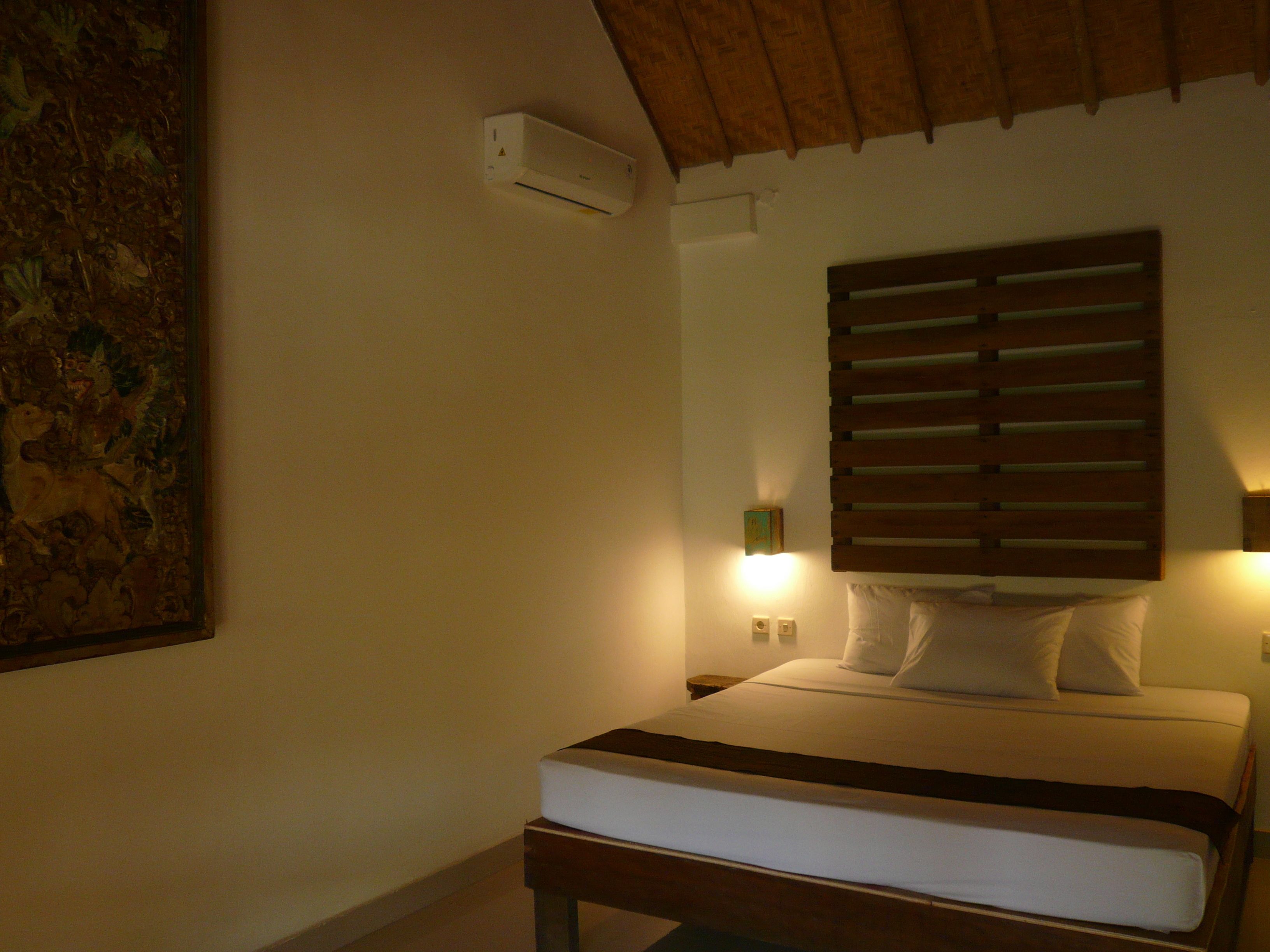 Una camera da letto con un letto, un comodino, un condizionatore d'aria a muro e un quadro appeso al muro.