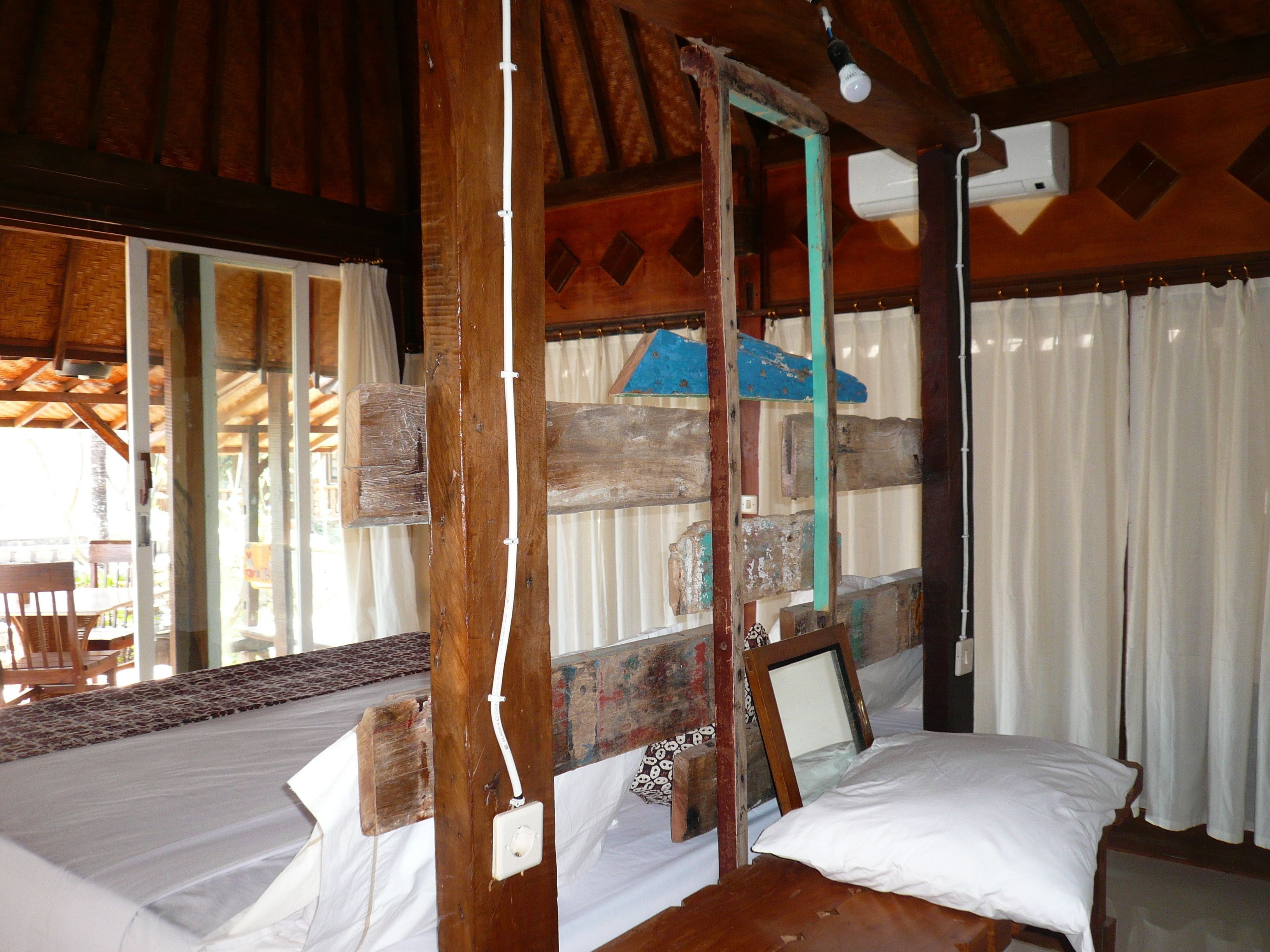 A rustic wooden room with a bed, a window with curtains, and a ceiling fan.
