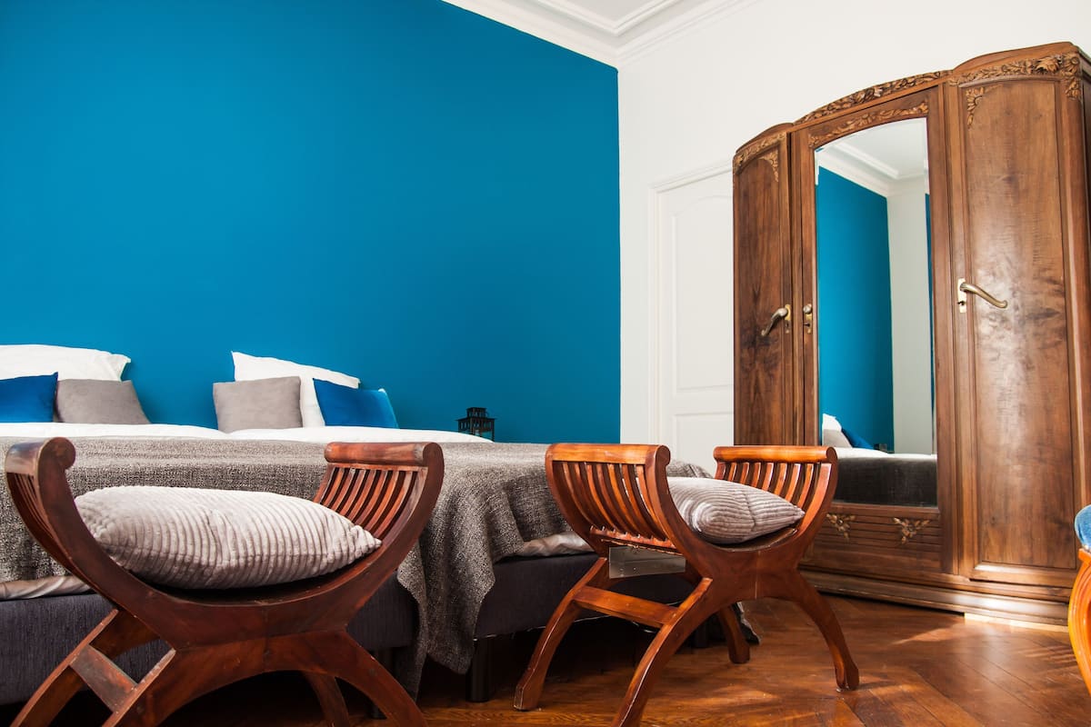 Une pièce avec un lit, deux chaises en bois, une armoire et un mur bleu.