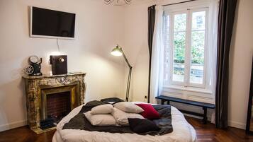Ein Schlafzimmer mit einem Bett, einem Kamin, einem Fernseher und einem Fenster mit Vorhängen.