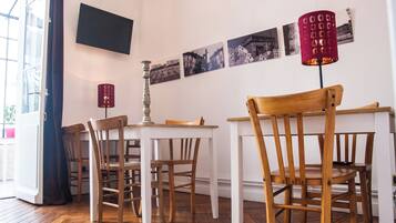 A dining area with wooden chairs and tables, a flat-screen TV mounted on the wall, and a series of black and white photographs displayed above the TV.